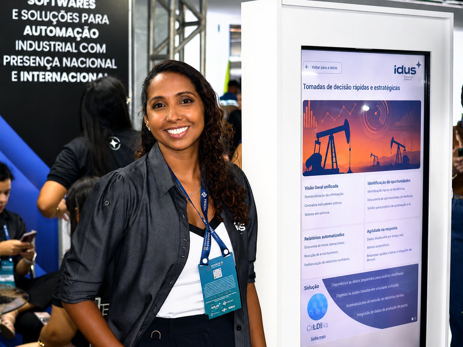 Profissional em espaço de demonstração da IDUS ao lado de painel com soluções industriais